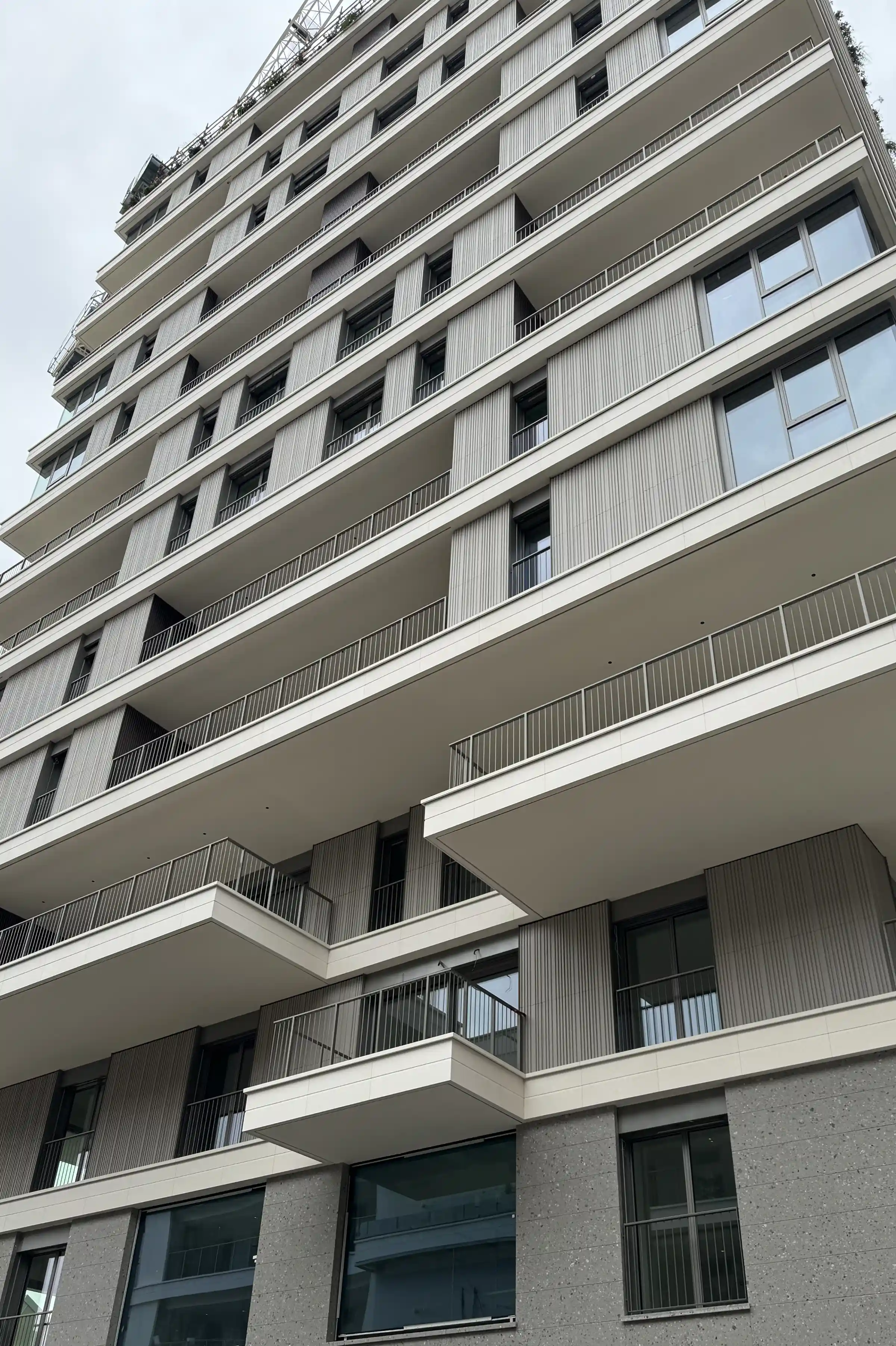 Vista dal basso della Torre Adamello Living Romana Yards a Milano: facciata con rivestimento in Agglotech SB130 Aggloceppo levigato, balconi a sbalzo con parapetti in acciaio e penthouse con terrazza panoramica - Trapattoni Marmi, Milano 2024-2025
