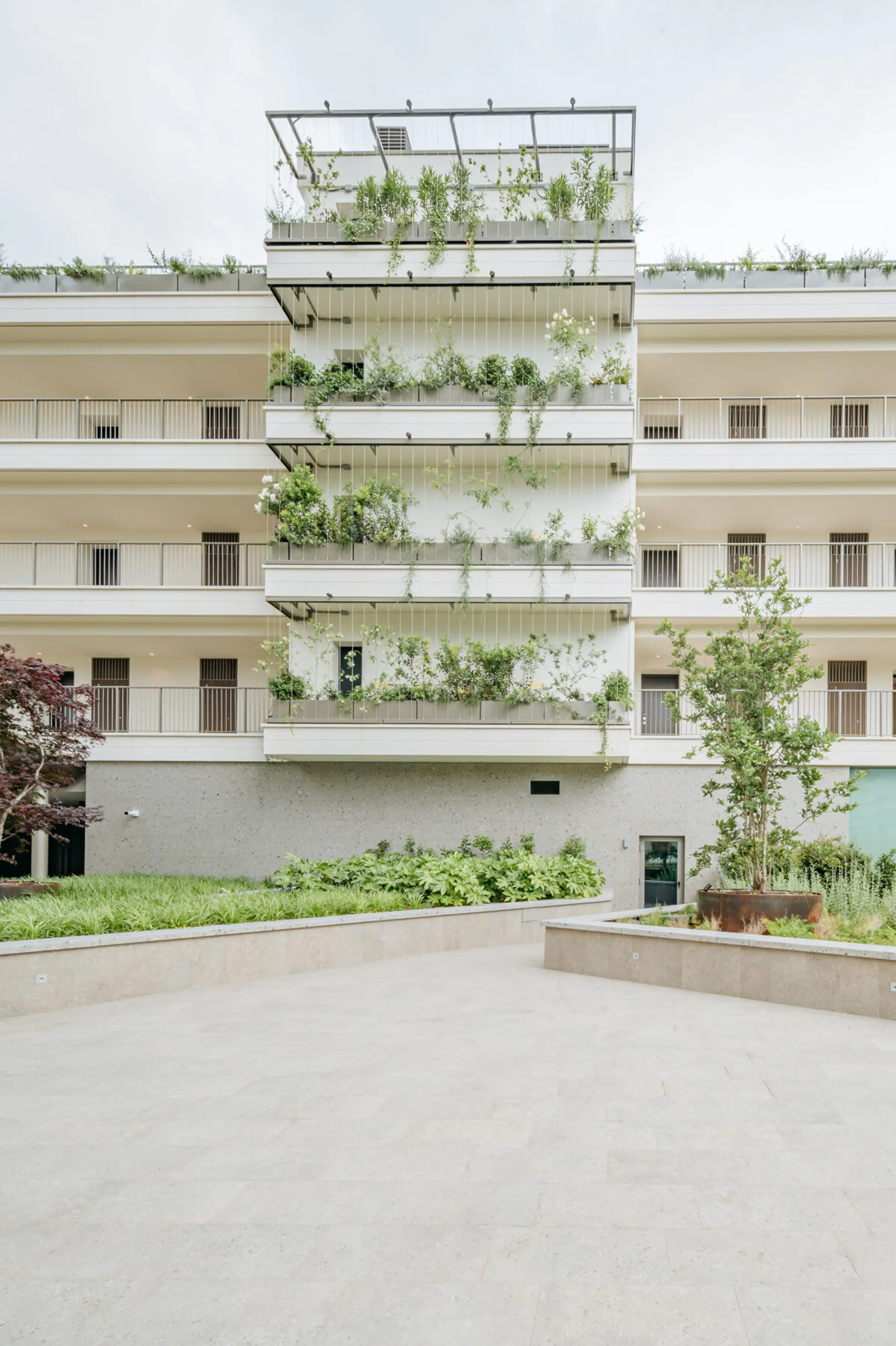 Cortile interno del complesso residenziale Adamello a Milano con facciata bassa in Agglotech SB130 Aggloceppo levigato, verde verticale pensile e pavimentazione in pietra naturale - posa in opera Trapattoni Marmi
