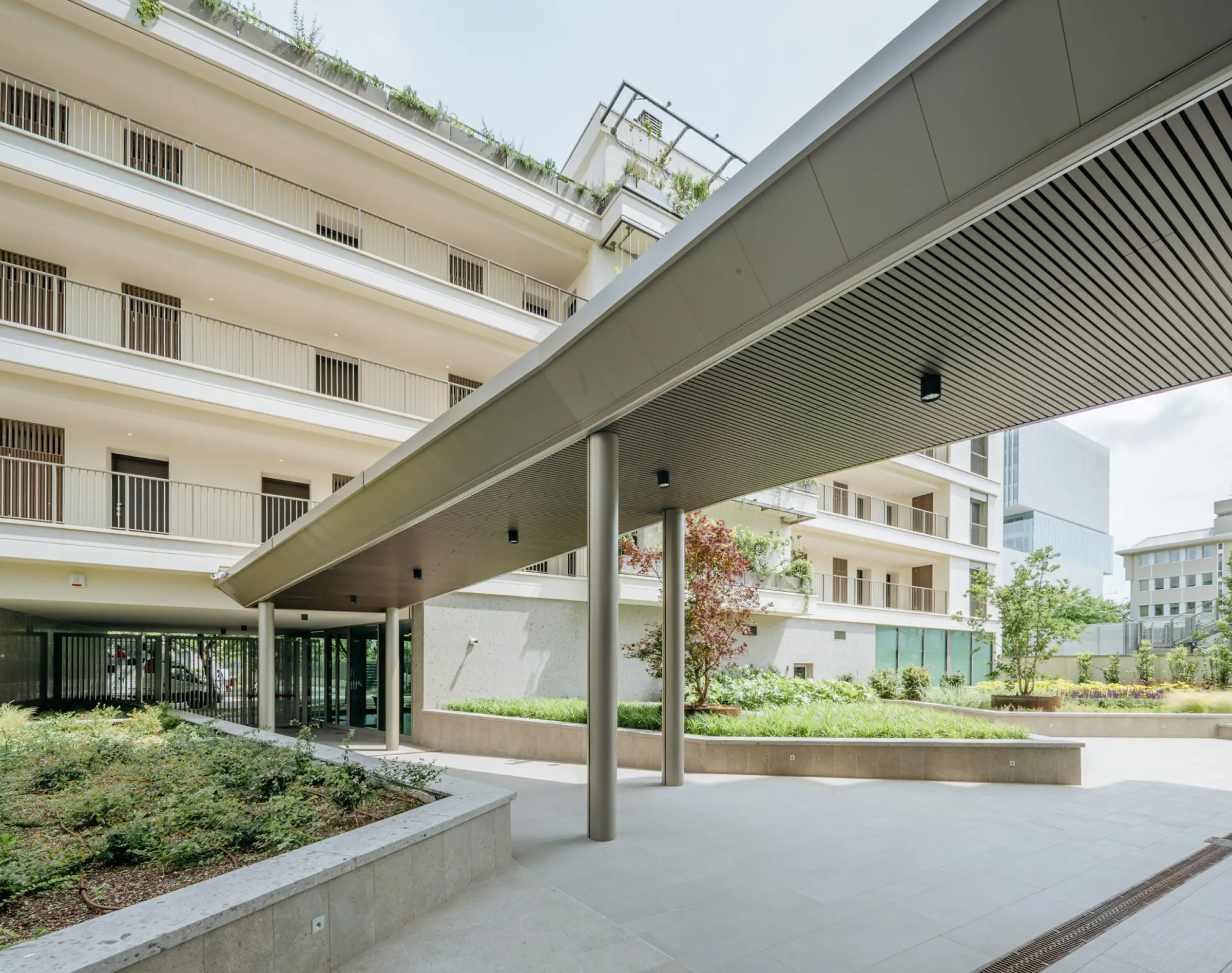 Portico d'ingresso del complesso Adamello Living Romana Yards a Milano con pensilina a sbalzo, pilastri in acciaio, pavimentazione in pietra naturale e corpo residenziale in Agglotech SB130 Aggloceppo levigato sullo sfondo - Trapattoni Marmi