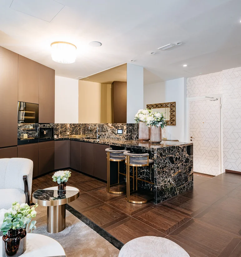 Cucina con isola, top e backsplash in Portoro, sgabelli in velluto e ottone, parete con mosaico geometrico bianco e specchio dorato - tea station dello studio dentistico Pinzuti vicino al Duomo di Milano, Trapattoni Marmi