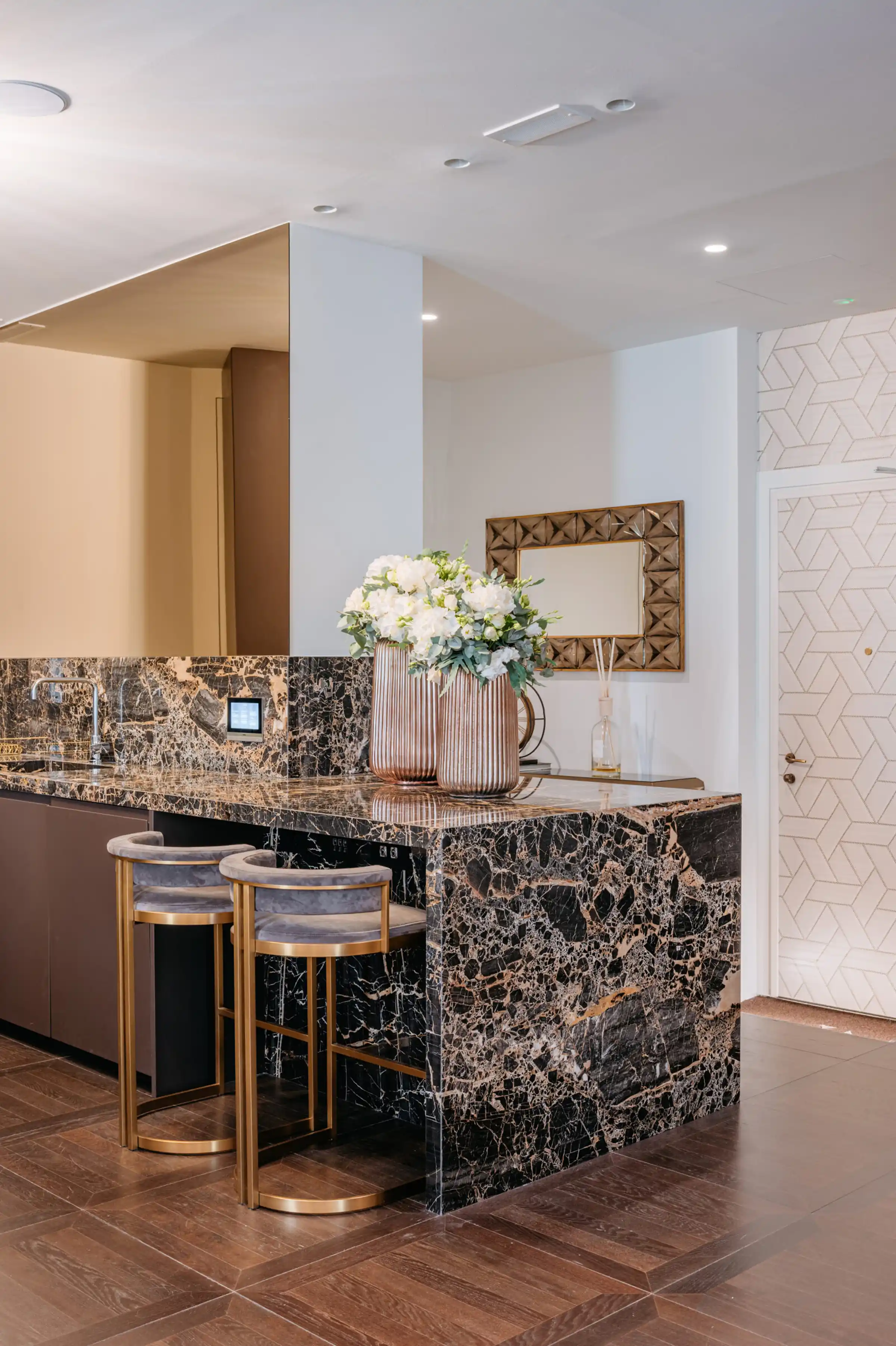 Isola cucina e piano in Portoro lucido con sgabelli in velluto grigio e ottone, vasi in rame con fiori bianchi e specchio con cornice dorata  tea station dello studio dentistico Pinzuti, posa in opera Trapattoni Marmi
