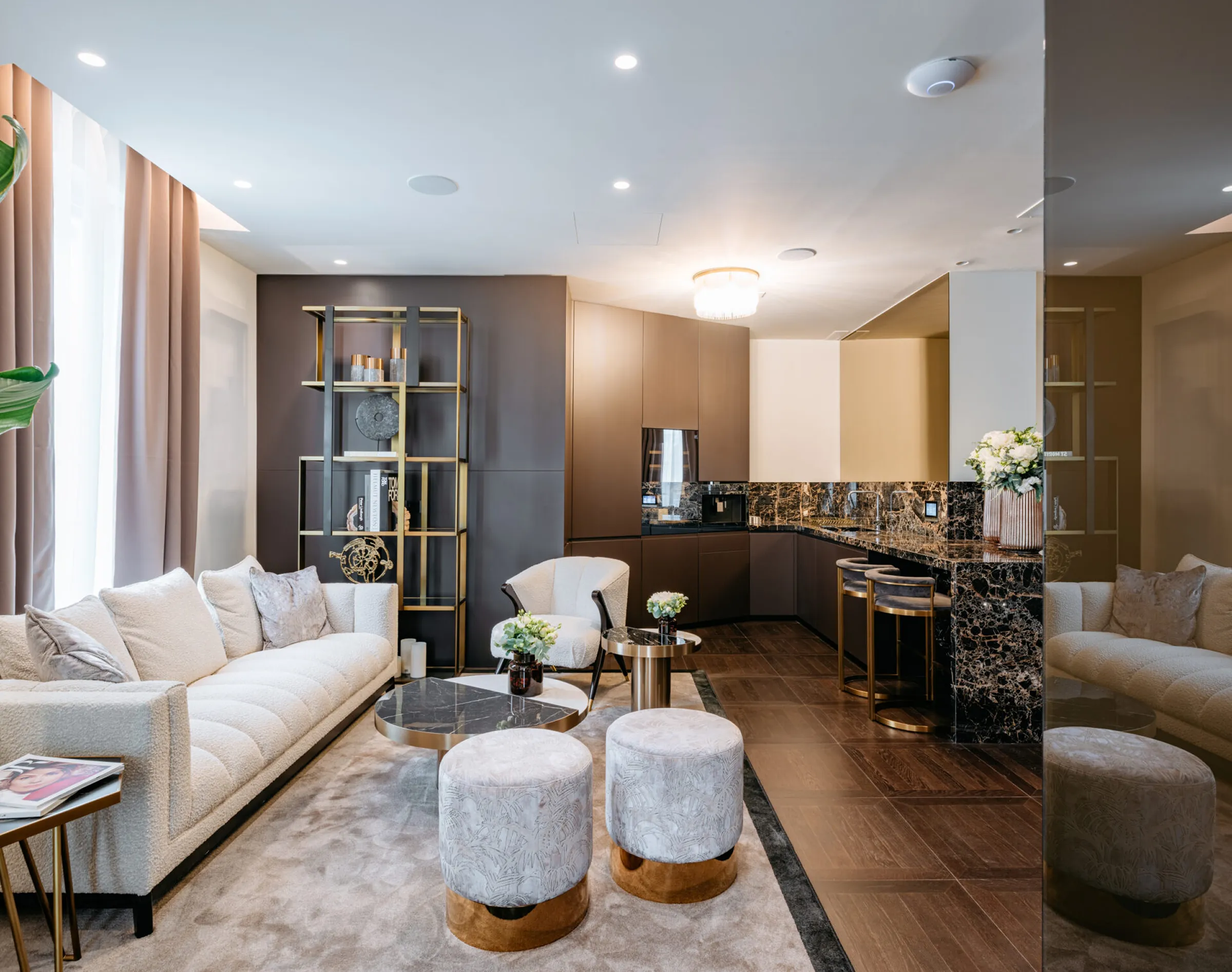 Zona living e cucina open space dello studio dentistico Pinzuti a Milano: divano bianco, pouf in tessuto, libreria dorata e isola in Portoro con sgabelli in ottone - interior luxury, lavorazione marmi Trapattoni Marmi