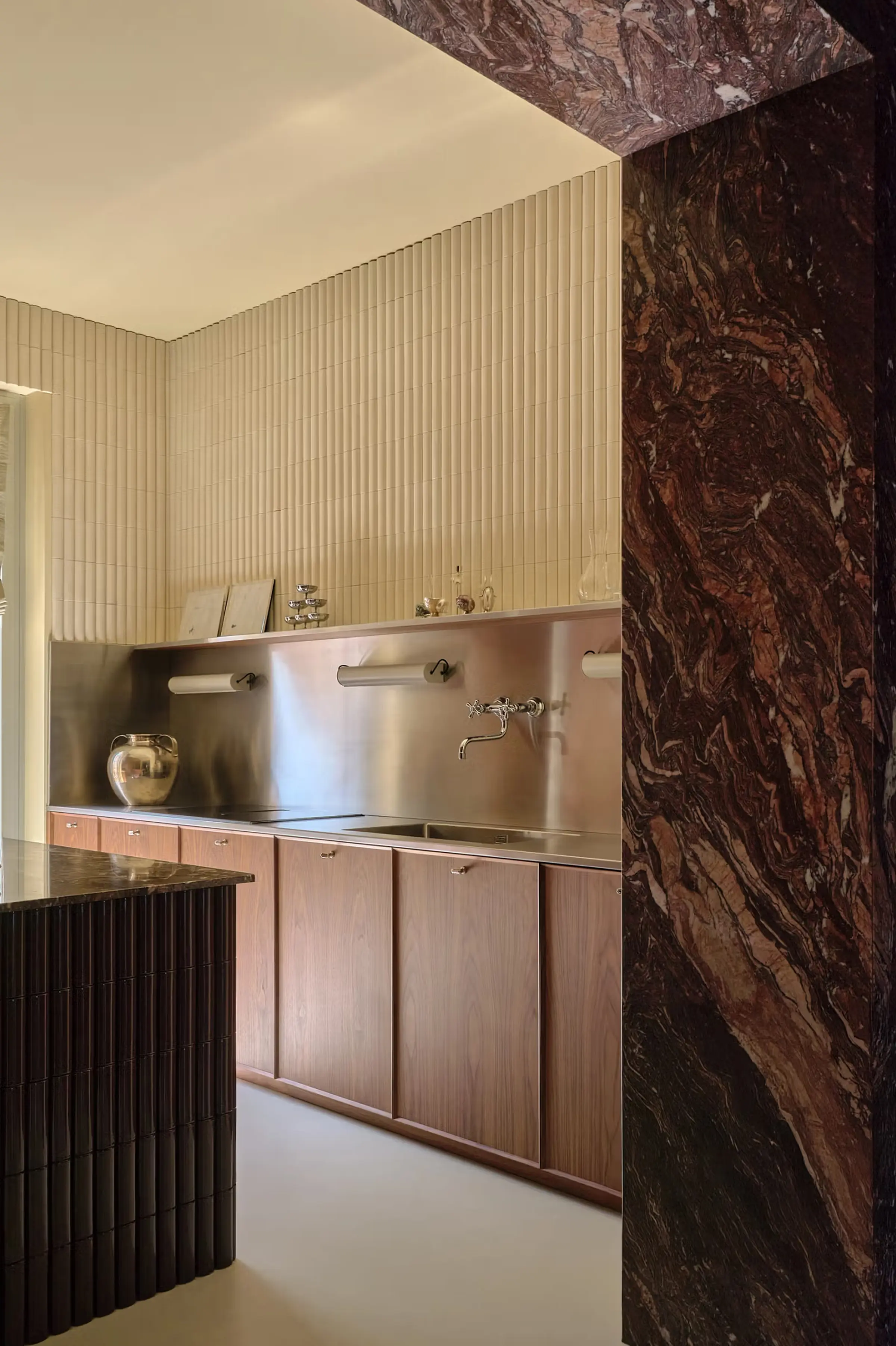 Cucina della dimora ai Navigli: piano cottura a induzione con backsplash in acciaio inox, mensole e mobili in noce Canaletto con maniglie in ottone, piano isola in Cipollino rosso-viola in primo piano - LC Atelier di Lucrezia Calvi x Trapattoni Marmi