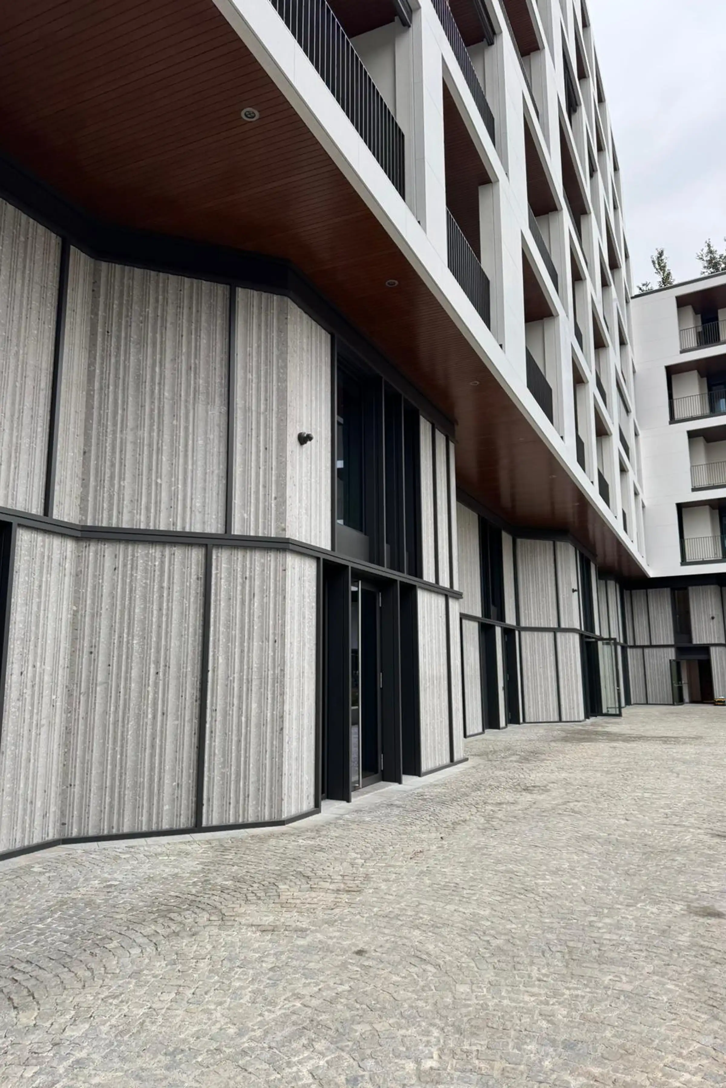 Ingresso del complesso Bosco Navigli con rivestimento verticale scanalato in Agglotech e soffitto in legno - lavorazione e posa Trapattoni Marmi Milano