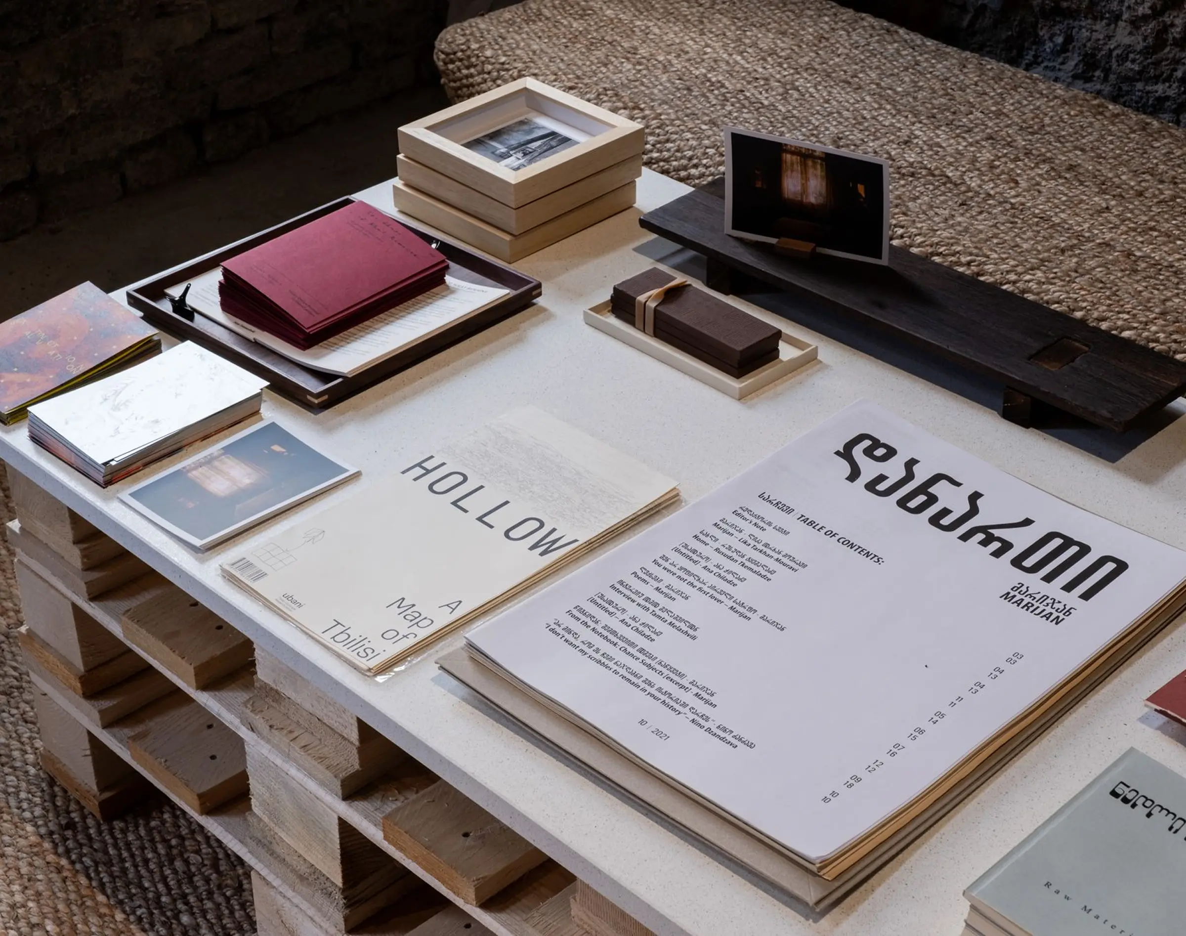 Tavolo espositivo con libri e pubblicazioni del collettivo Aea Cultural Initiative nell'installazione The Shape of What Remains alla Biennale del Design di Venezia 2025 - con il supporto di Trapattoni Marmi