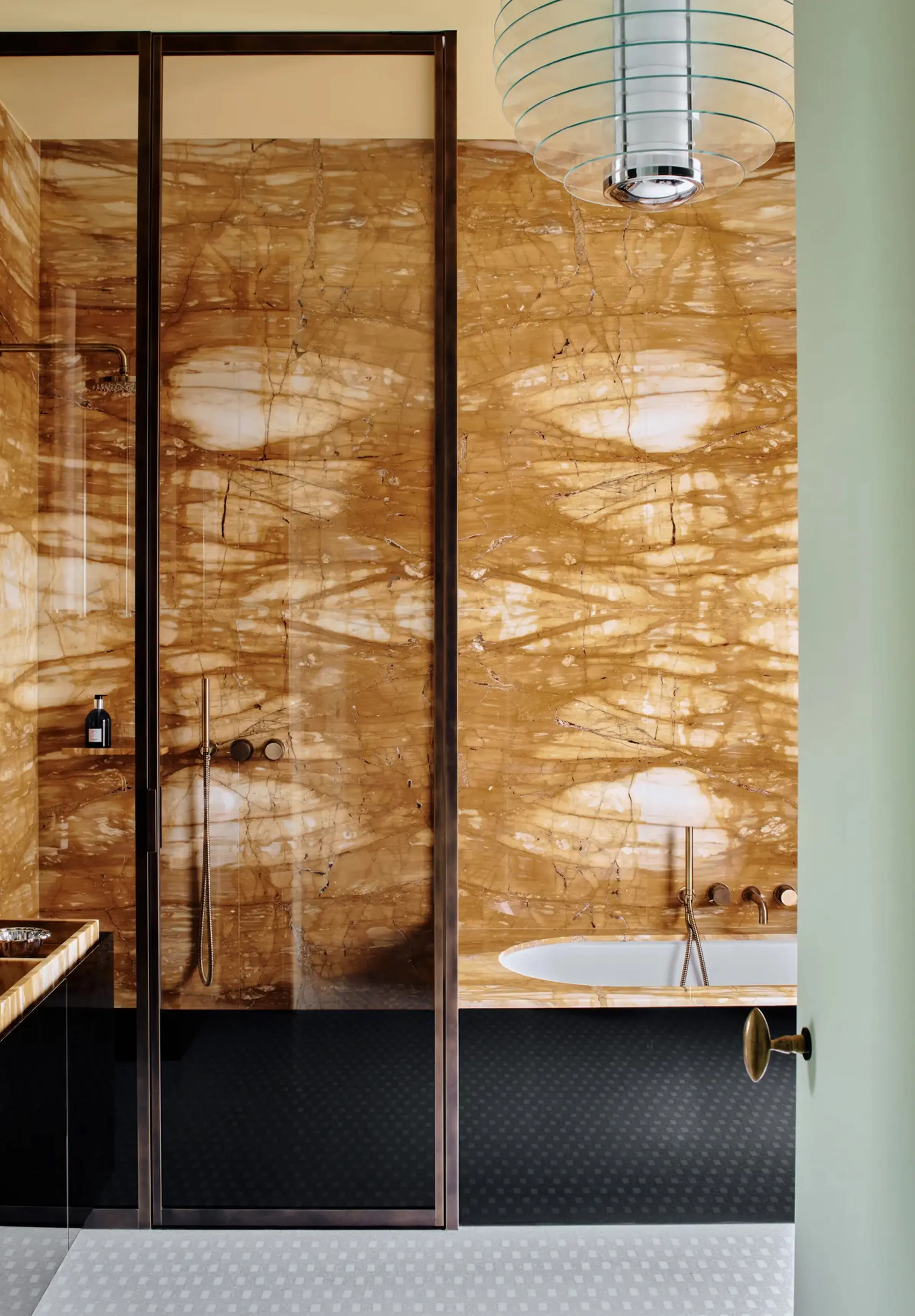 Rivestimento a macchia aperta in Giallo Siena lucido con venature ambrate nel bagno master del progetto LC Castello: box doccia con profili in bronzo, vasca integrata con rubinetteria in ottone e pavimento in mosaico bianco – LC Atelier, lavorazione artigianale marmi Trapattoni Marmi